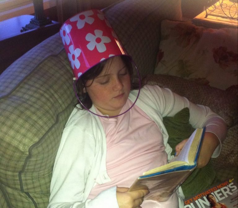 Mary Claire Wearing a Flowered Bucket on Her Head While Reading